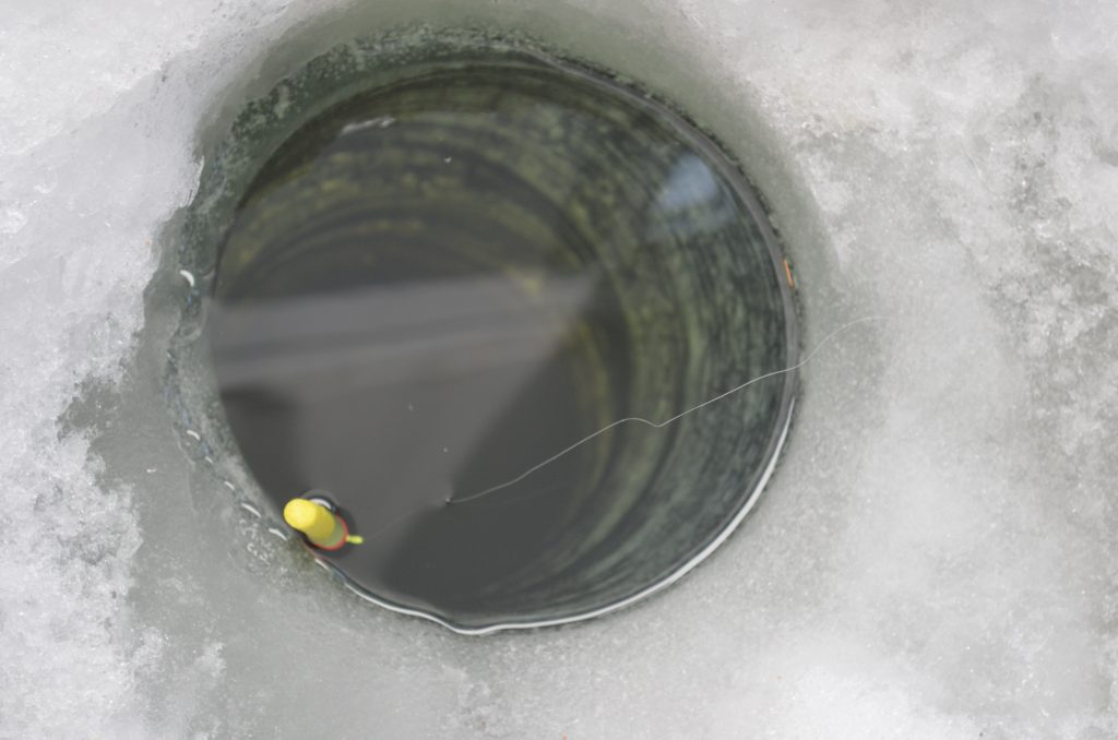 Bobber floating in an ice hole from a fish house on Lake of the Woods MN