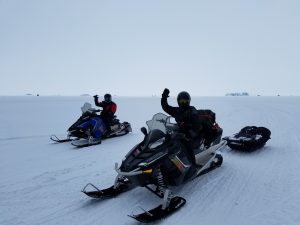 snowmobilers on a lake trail with collapsible fish house