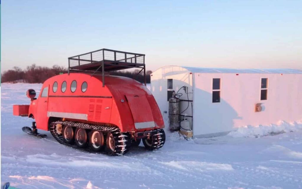 A bright rerd Bombardier sits next to a fish house on Lake of the Woods
