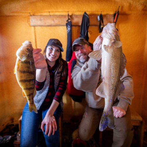 Jen Pudenz and Bret Amundson with a jumbo perch and walleye inside a Lake of the Woods MN fish house, full service ice fishing