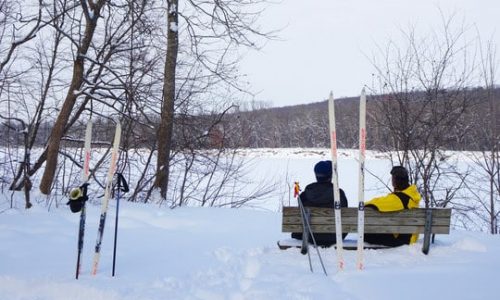 cross country skiiers rest on a bench in the woods next to lake of the woods