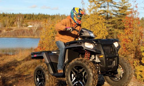 A man is riding his ATV on a trail near Lake of the Woods that is surrounded by fall colors.
